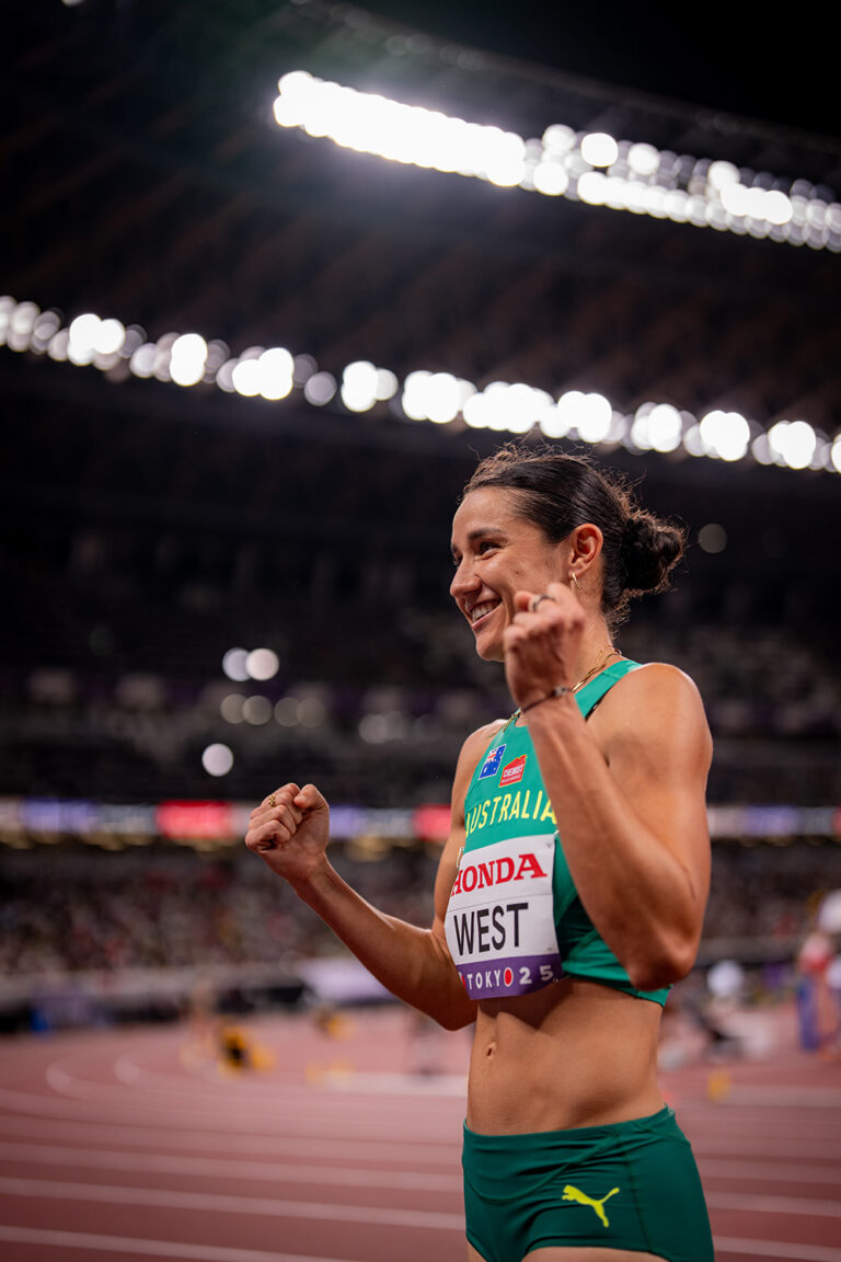 Australian sprinter celebrates with clenched fists on a running track under stadium lights, after a race.