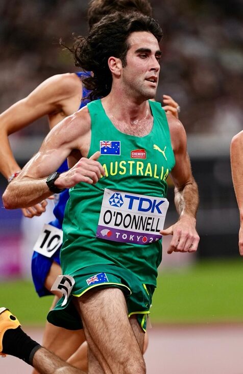 Australian sprinter in a green Australia kit runs on a track; bib reads O'DONNELL, Tokyo 2020 (Olympics).