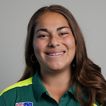 Portrait of a smiling woman with long brown hair wearing a green polo shirt with an Australian flag patch.