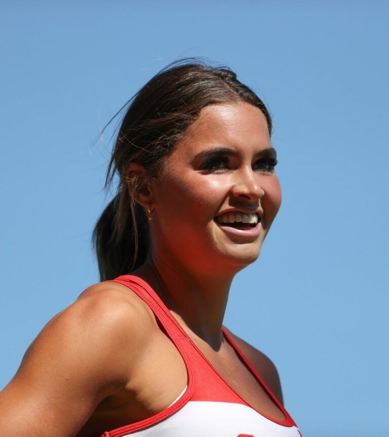 Smiling woman in a red and white athletic top outdoors against a clear blue sky