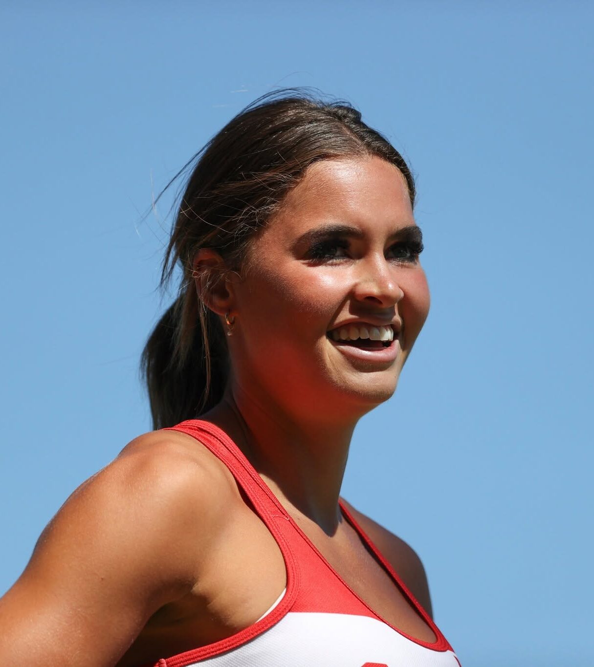 Smiling woman in a red and white athletic top outdoors against a clear blue sky
