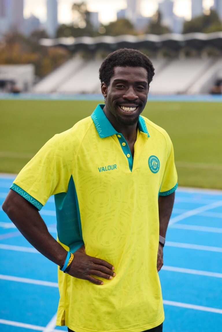 Smiling man in a bright yellow and teal polo on a running track, posing for a photo.