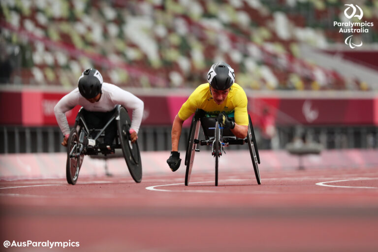 Wheelchair sprinter in a yellow jersey powers forward on a track, helmet on, focused on the race.