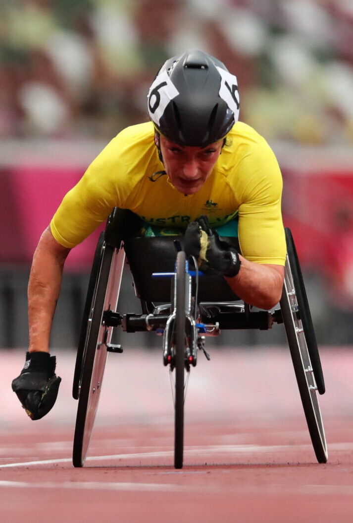 Wheelchair sprinter in a yellow jersey powers forward on a track, helmet on, focused on the race.