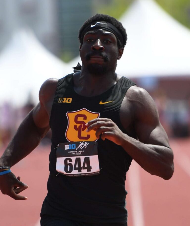 Two male sprinters race on a track; one in black USC uniform with bib 644 leads, the other in yellow nearby.