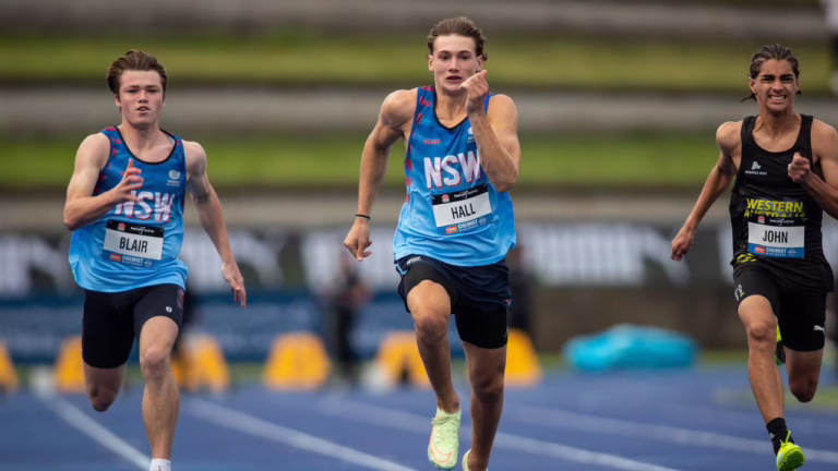 Young male athlete in a blue NSW running singlet sprinting toward the camera, pointing a finger as he runs; bib reads 'HALL'.
