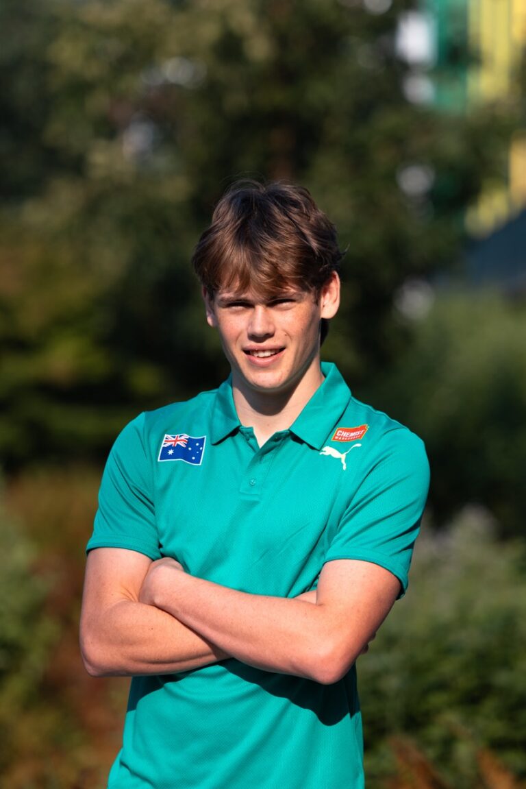 Young man outdoors with arms crossed, wearing a teal polo shirt with an Australian flag patch and a Puma logo.