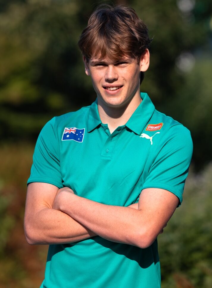 Young man outdoors with arms crossed, wearing a teal polo shirt with an Australian flag patch and a Puma logo.