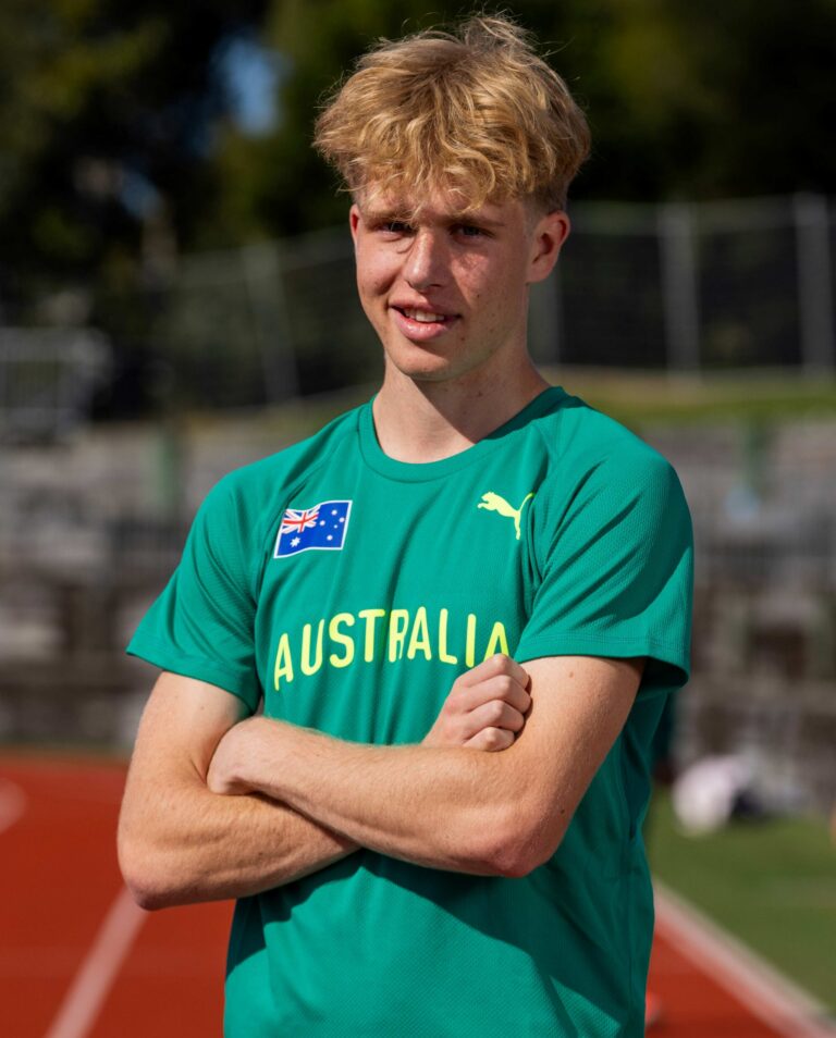 Young man in a green Australia jersey on a running track, arms crossed.