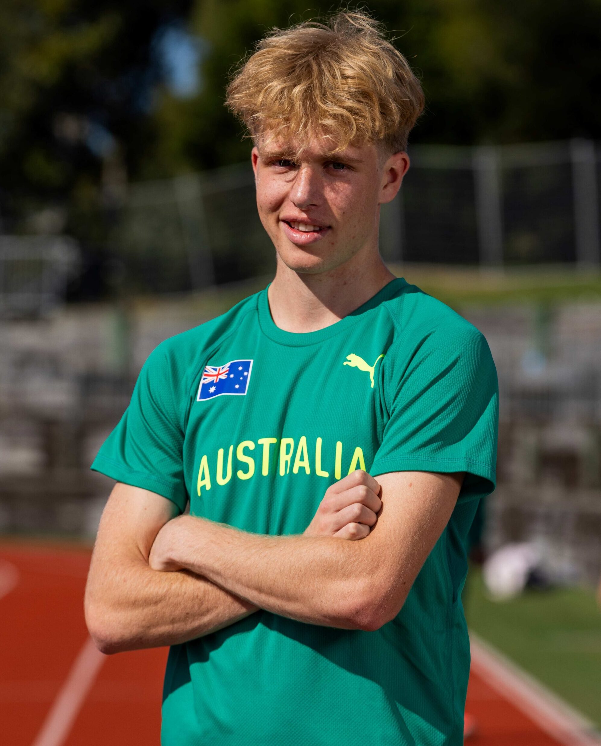 Young man in a green Australia jersey on a running track, arms crossed.