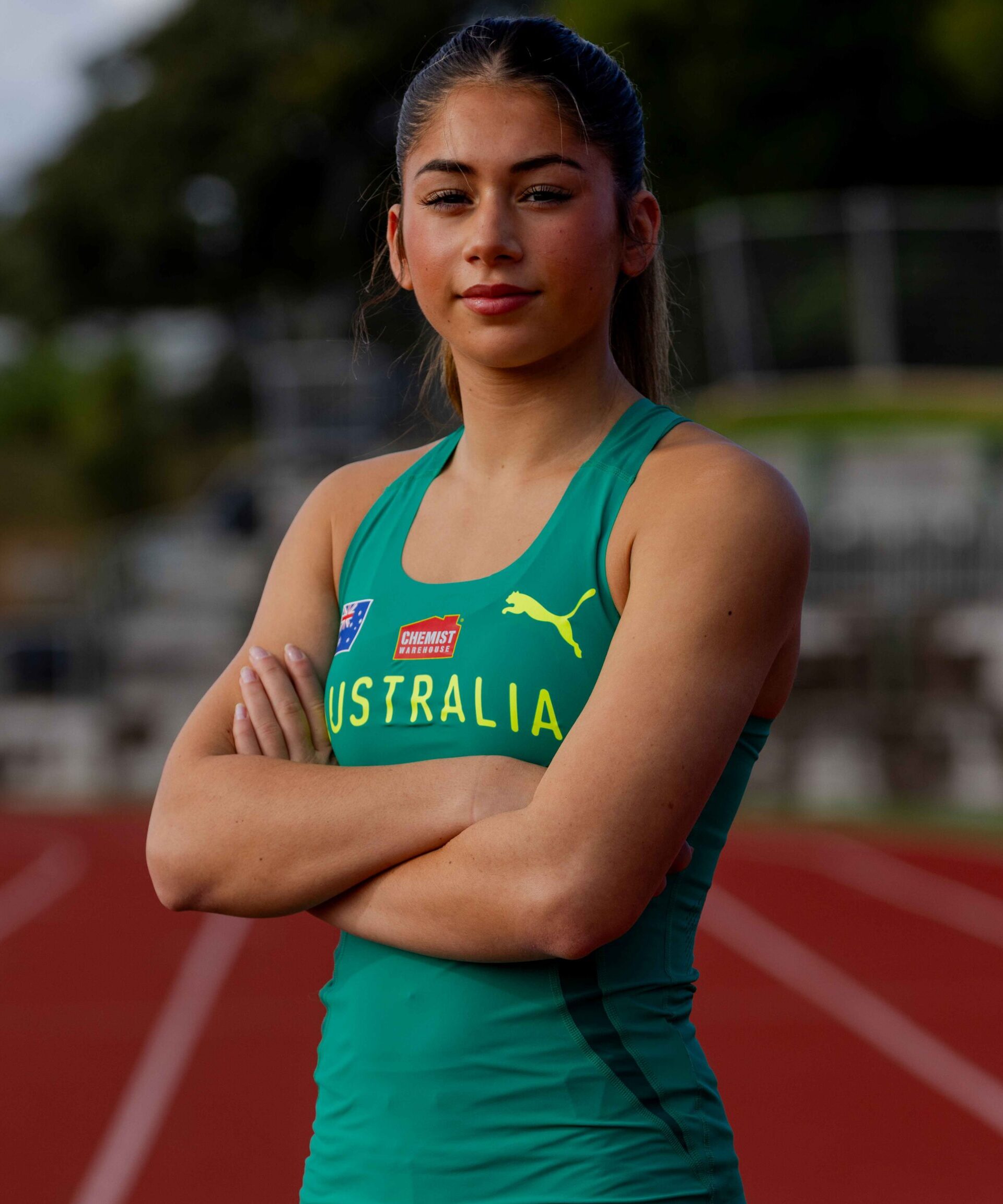 Australian female athlete standing on a track with arms crossed, wearing a teal Australia uniform.