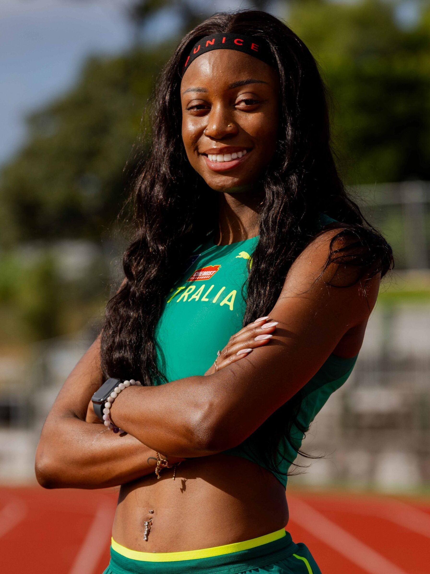 Smiling female athlete in a teal-green sprint uniform, standing with arms crossed on a track field.