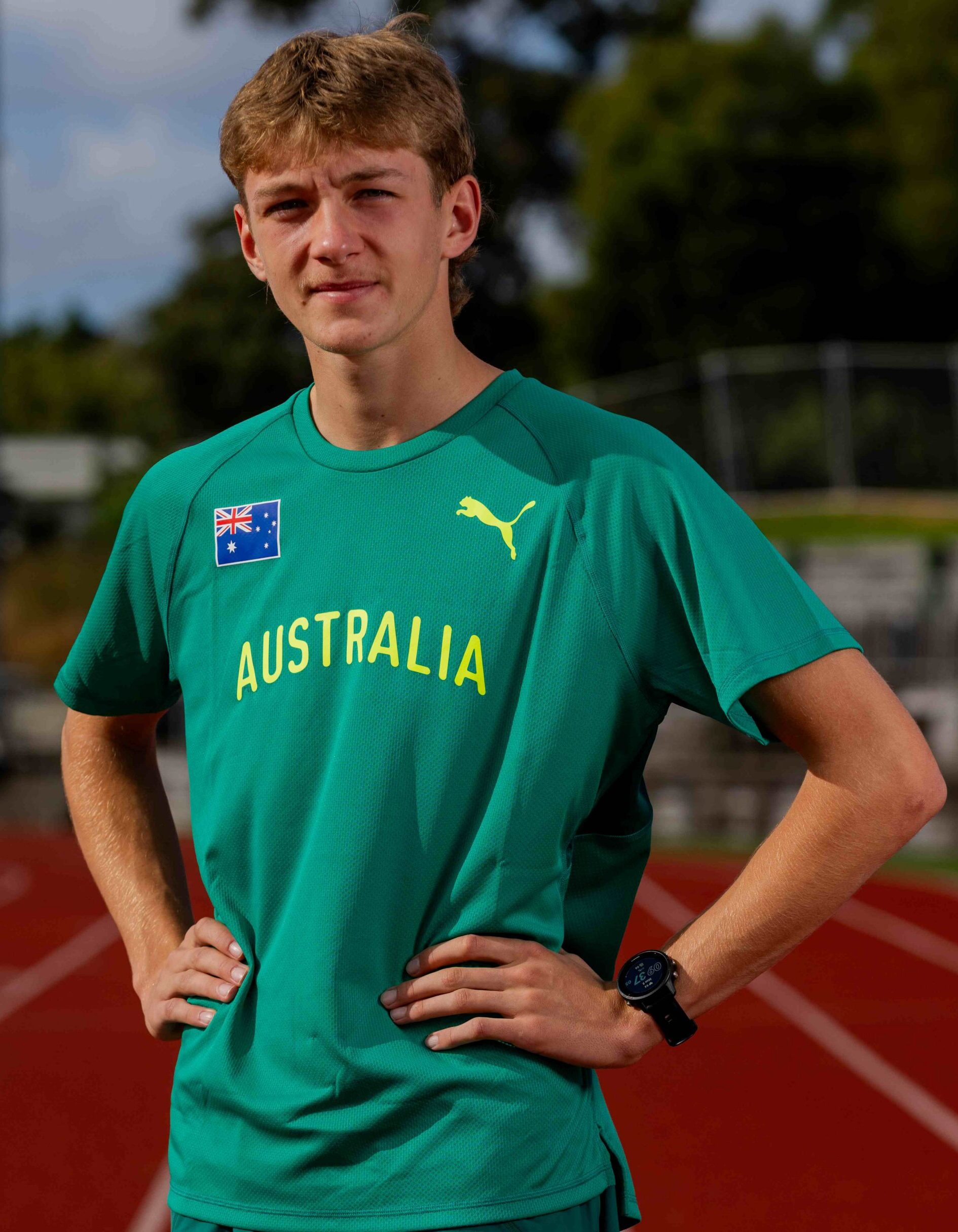 Athlete wearing a green Australia shirt standing on a running track with hands on hips.