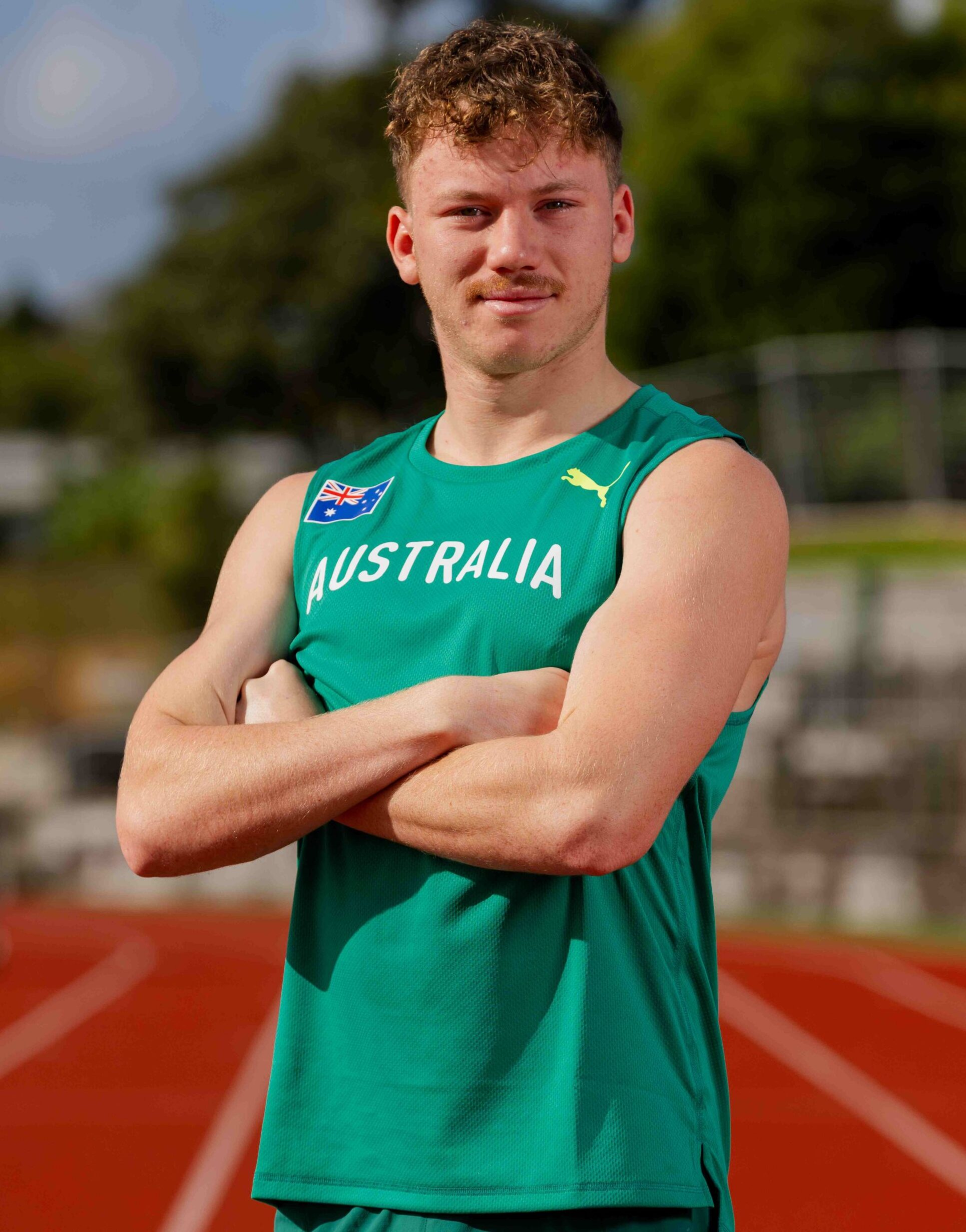 Athlete wearing green Australia uniform with arms crossed on a running track, looking at camera.