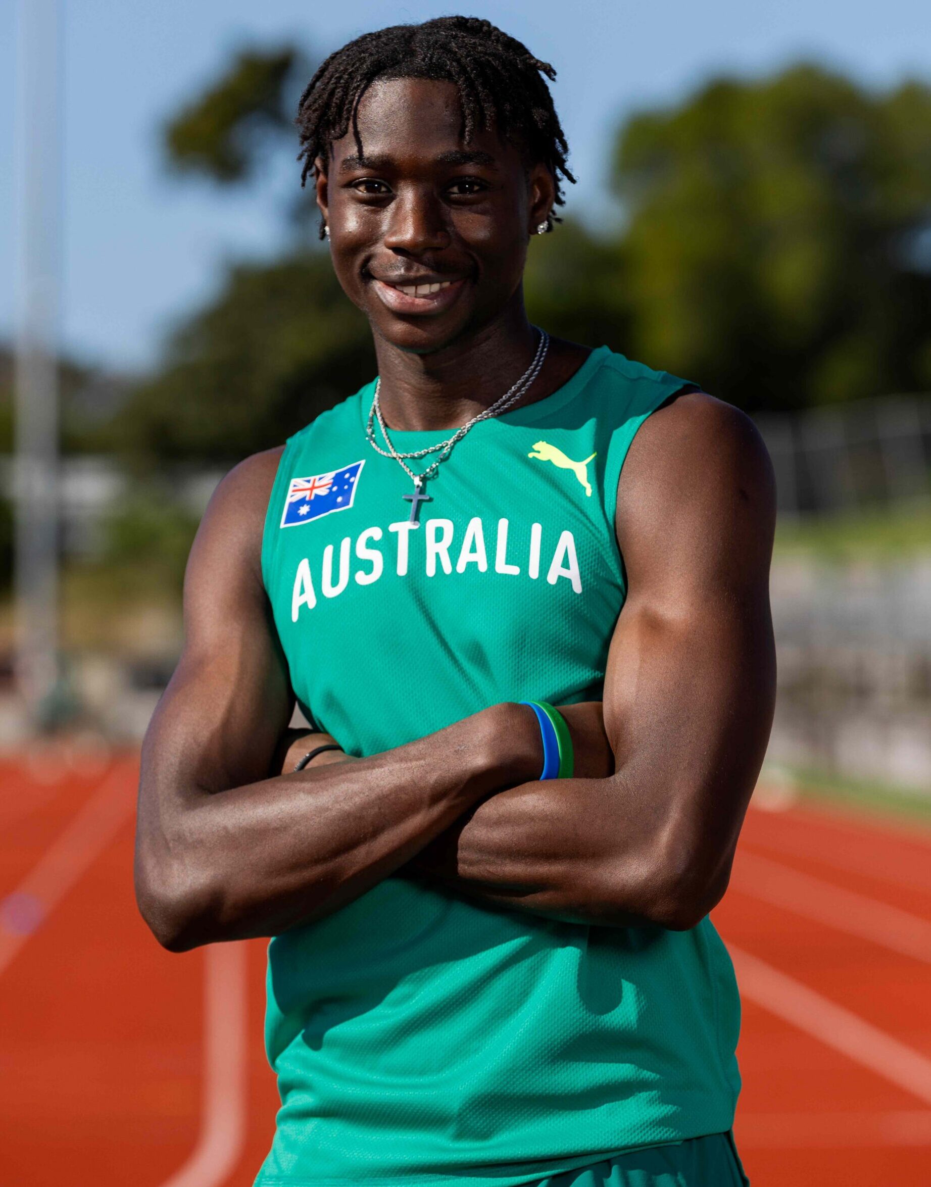 Smiling athlete in a teal Australia uniform standing on a running track.